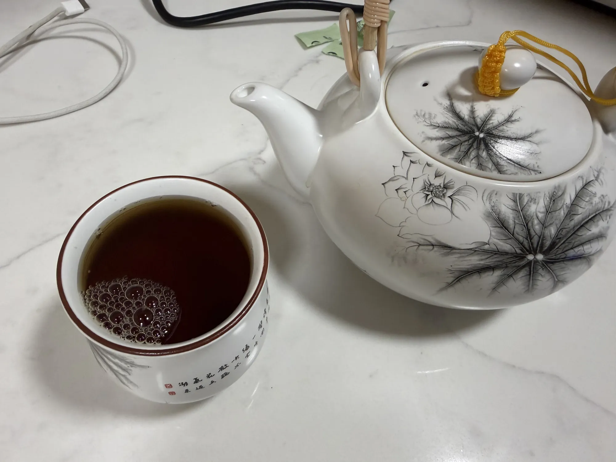 The same teapot and cup, this time filled with dark brown coffee, foam still sitting on top